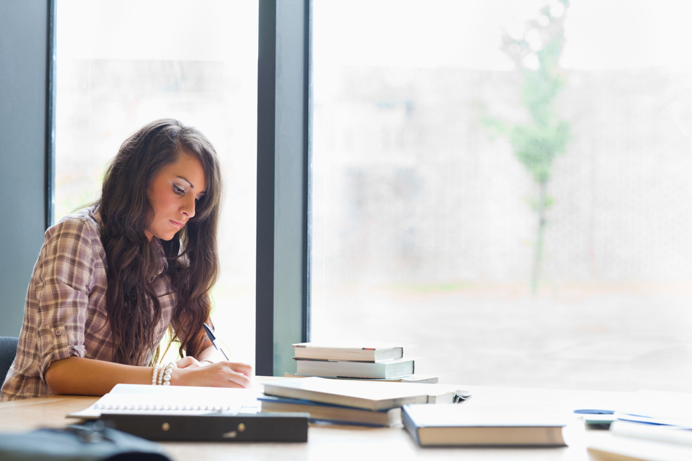 Beautiful student writing an essay in a library